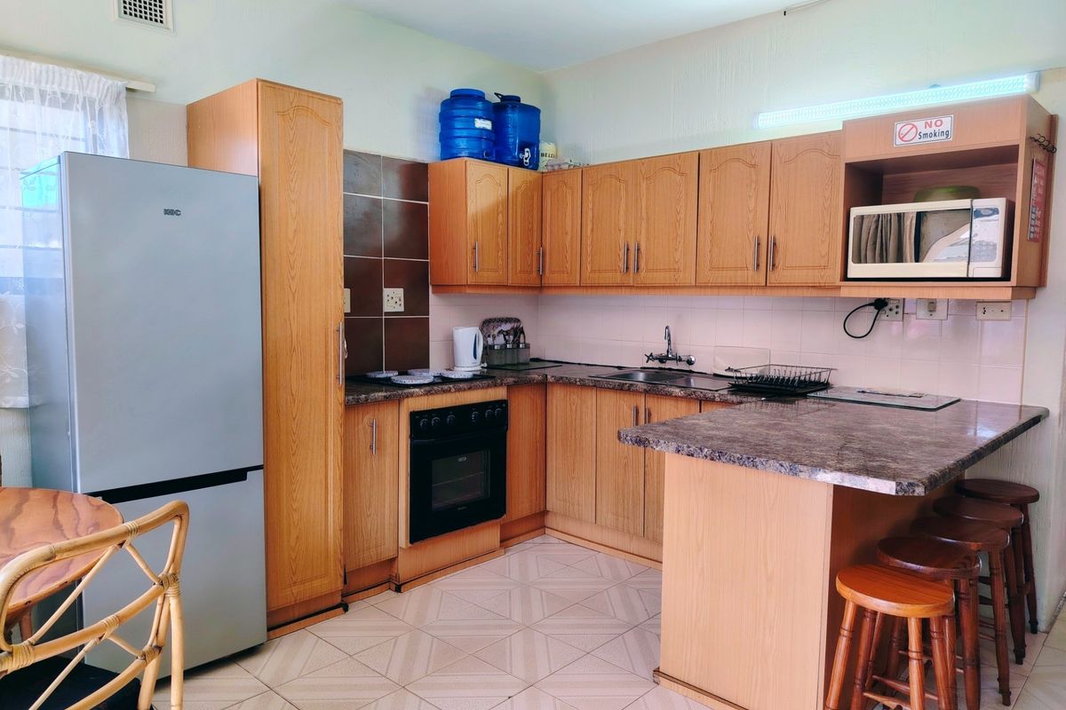 A functional kitchen featuring wood-finish cabinetry, laminate countertops, a built-in oven, and a breakfast nook with tiled flooring throughout.