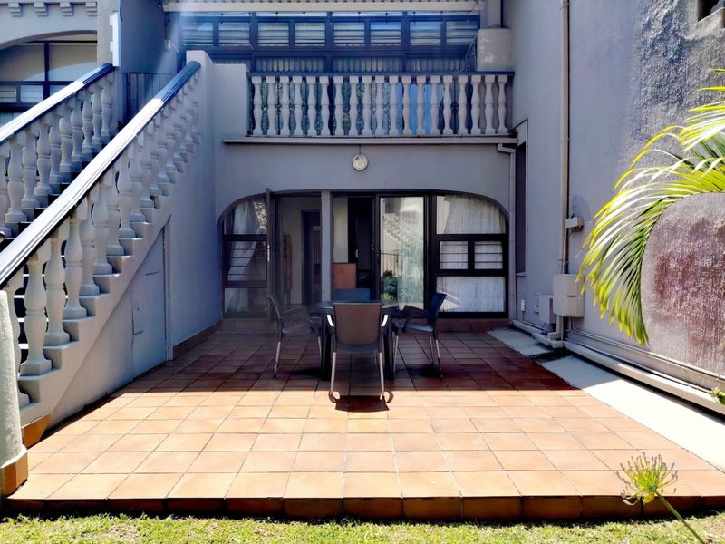 A private tiled patio area featuring an external staircase, concrete balustrades, and direct access to the interior through sliding glass doors.