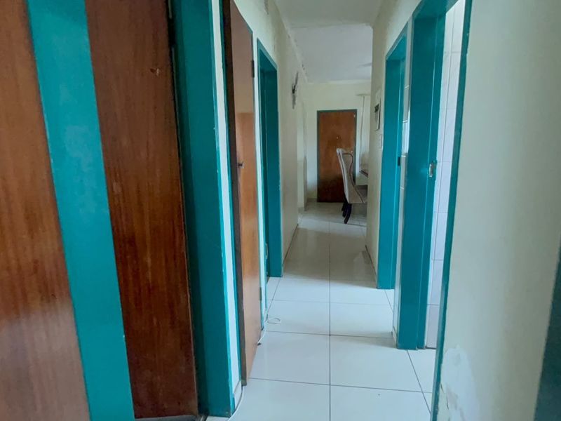 A functional hallway featuring tiled flooring and multiple wooden doors with painted frames, showing signs of wear and requiring cosmetic updates.