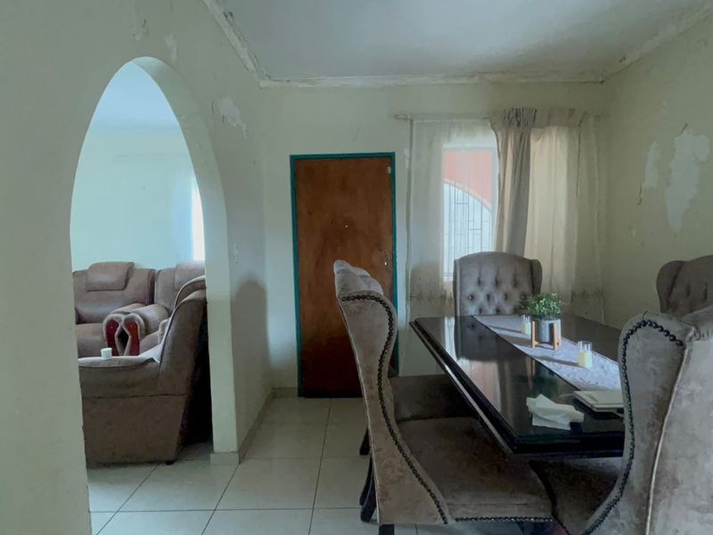 Dining area featuring an arched entryway and tiled flooring, currently showing significant signs of wear including peeling paint on the walls and ceiling.