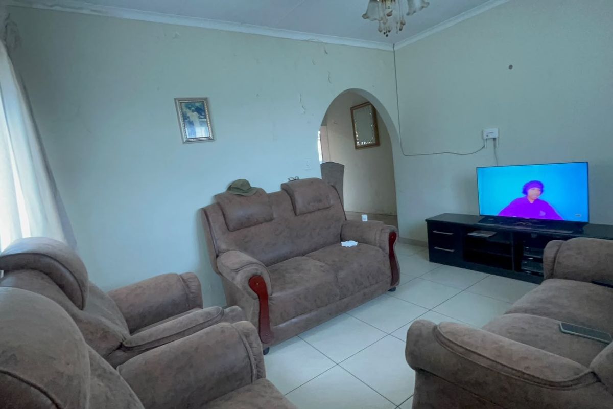 A living room featuring tiled flooring and an arched doorway, showing visible signs of wall plaster damage and paint deterioration.
