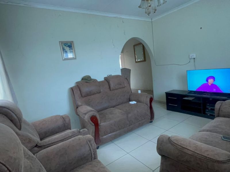 A living room featuring tiled flooring and an arched doorway, showing visible signs of wall plaster damage and paint deterioration.