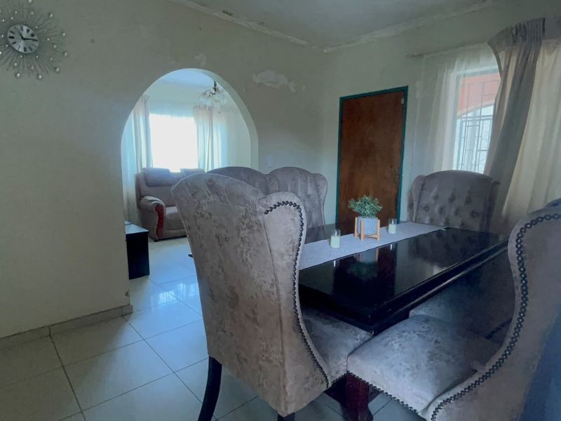 Dining room featuring tiled flooring and an arched entryway leading to an adjacent living space, showing signs of wear on the ceiling and walls.