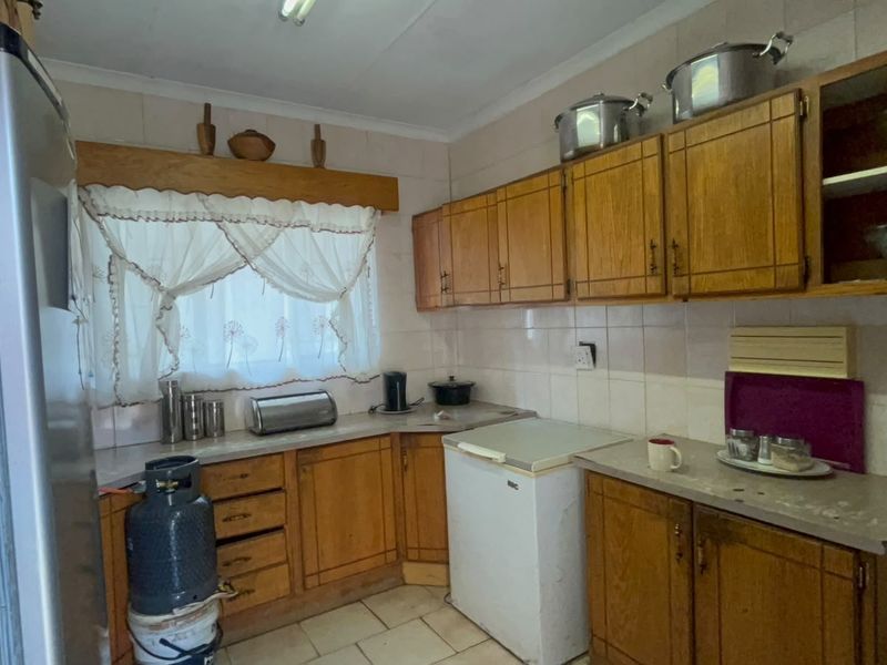 A dated kitchen featuring wooden cabinetry, laminate countertops, and tiled backsplash, offering potential for a modern renovation.