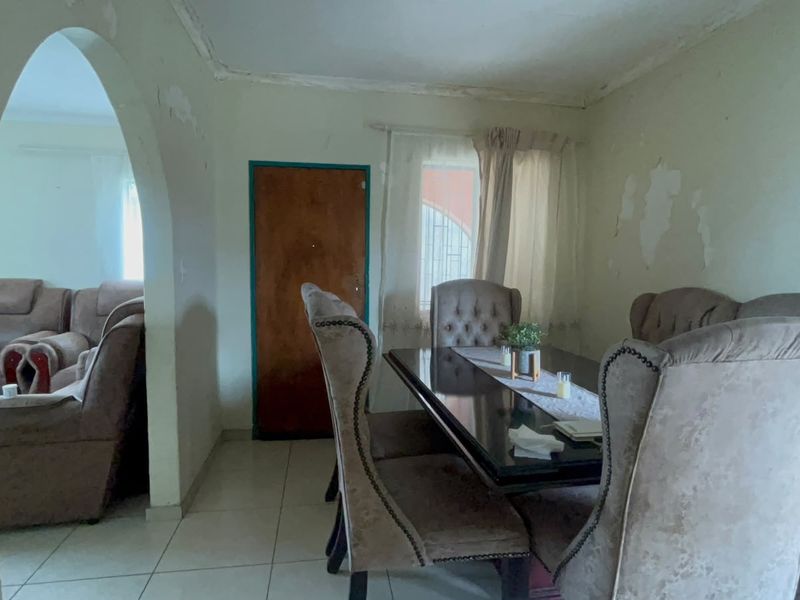 Dining room featuring tiled flooring and an arched entryway, currently showing significant wear to wall and ceiling finishes requiring maintenance.