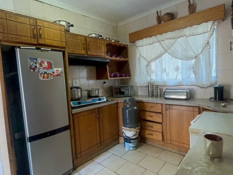A dated kitchen featuring wooden cabinetry, tiled backsplash, and tiled flooring, offering a functional layout with potential for modern renovation.