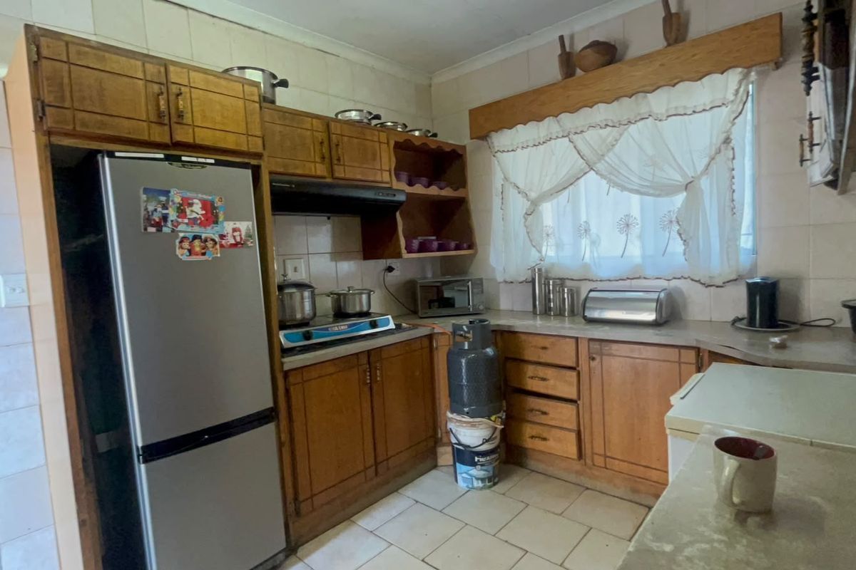 A dated kitchen featuring wooden cabinetry, tiled backsplash, and tiled flooring, offering a functional layout with potential for modern renovation.
