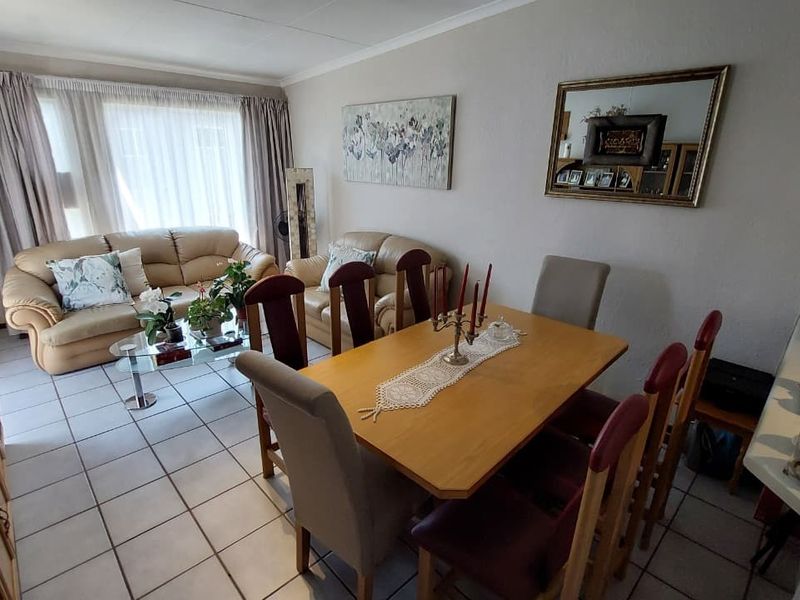 An open-plan living and dining area featuring neutral wall finishes, tiled flooring, and large windows with curtain tracks.