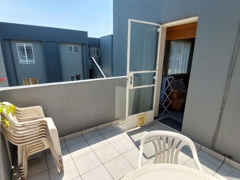 A private balcony featuring tiled flooring, a security gate with an integrated pet door, and views of the surrounding townhouse complex.