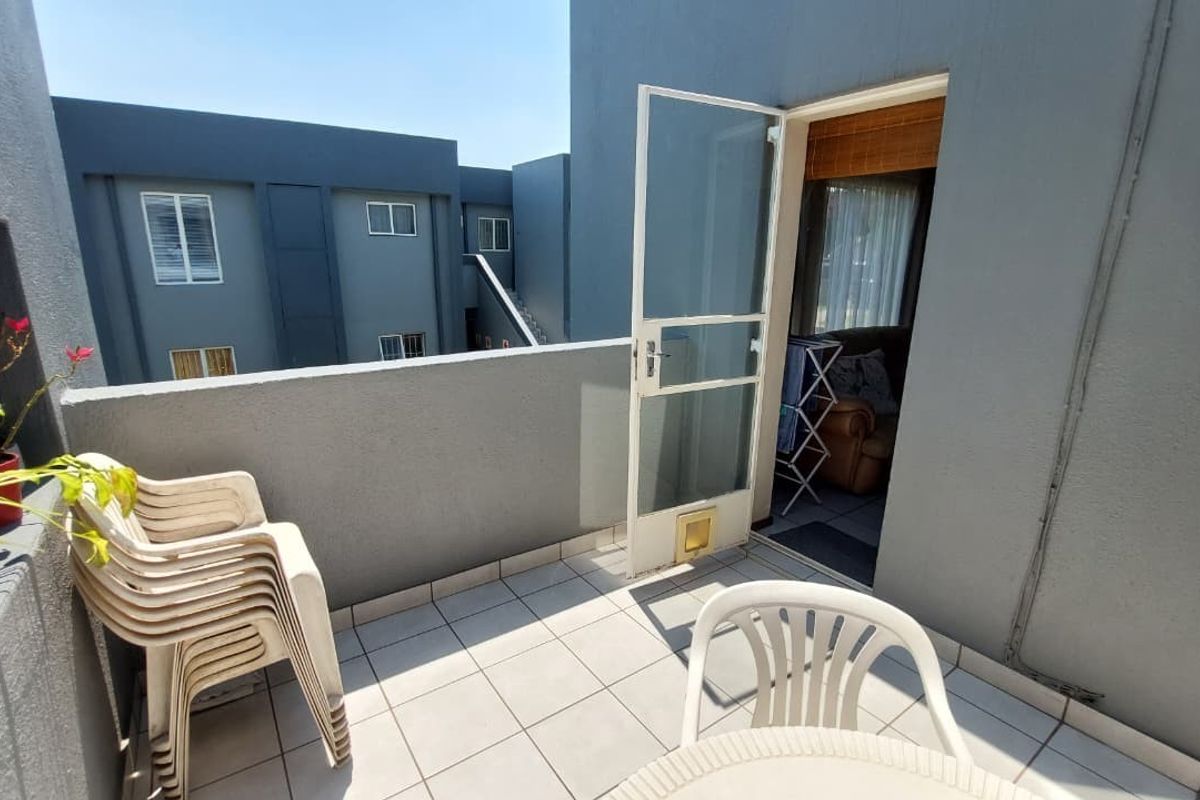 A private balcony featuring tiled flooring, a security gate with an integrated pet door, and views of the surrounding townhouse complex.