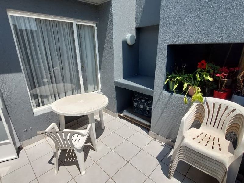 A compact outdoor patio area featuring tiled flooring and a built-in braai, providing a functional space for outdoor relaxation and entertaining.
