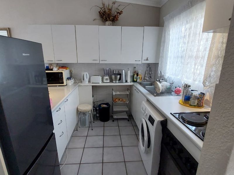 A functional kitchen featuring white cabinetry, laminate countertops, a stainless steel sink, and integrated electric cooking appliances with tiled flooring.