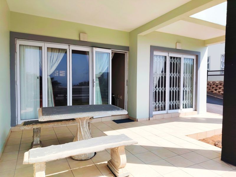 A covered patio area featuring tiled flooring, sliding glass doors with security gates, and wall-mounted lighting, providing direct access to the interior living space.