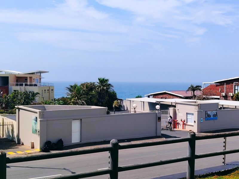 Street view of the apartment complex entrance featuring perimeter walls, security gate, and ocean views in the background.