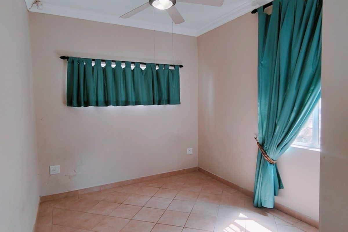 An empty bedroom featuring tiled flooring, a ceiling fan, and neutral wall finishes, providing a blank canvas for personalization.