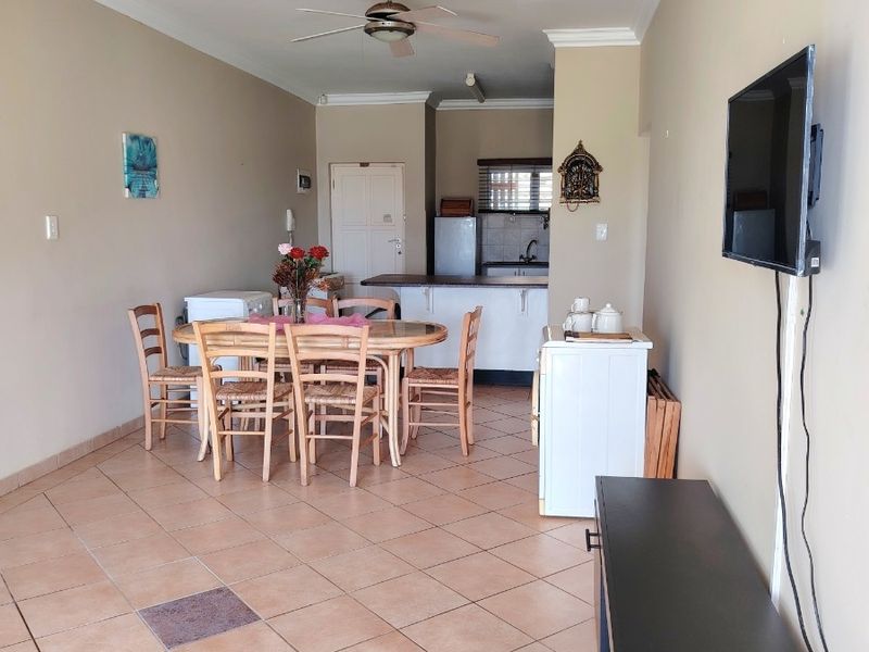 Open plan living and dining area featuring tiled flooring, a ceiling fan, and a functional kitchen space with built-in cabinetry.
