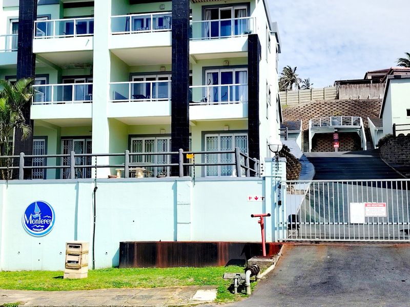 Front elevation of the Monterey apartment complex featuring multi-level balconies with glass balustrades, secure gated access, and a paved driveway.