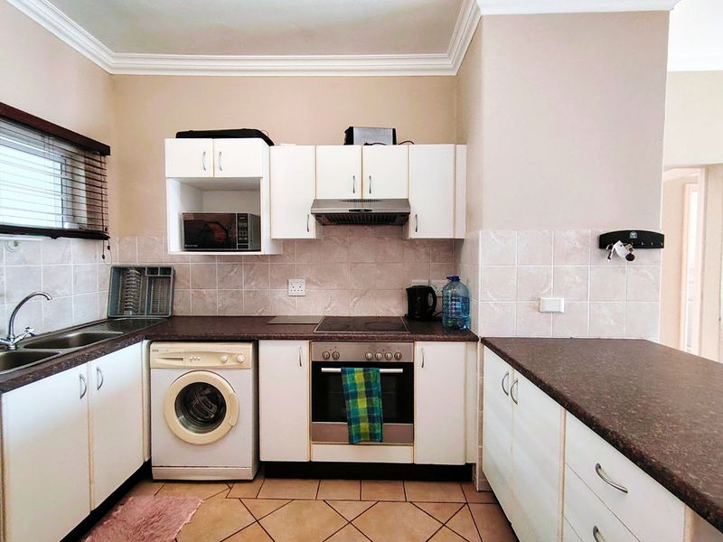A functional kitchen featuring white cabinetry, dark laminate countertops, tiled backsplash, and integrated appliances including an oven, hob, and extractor fan.
