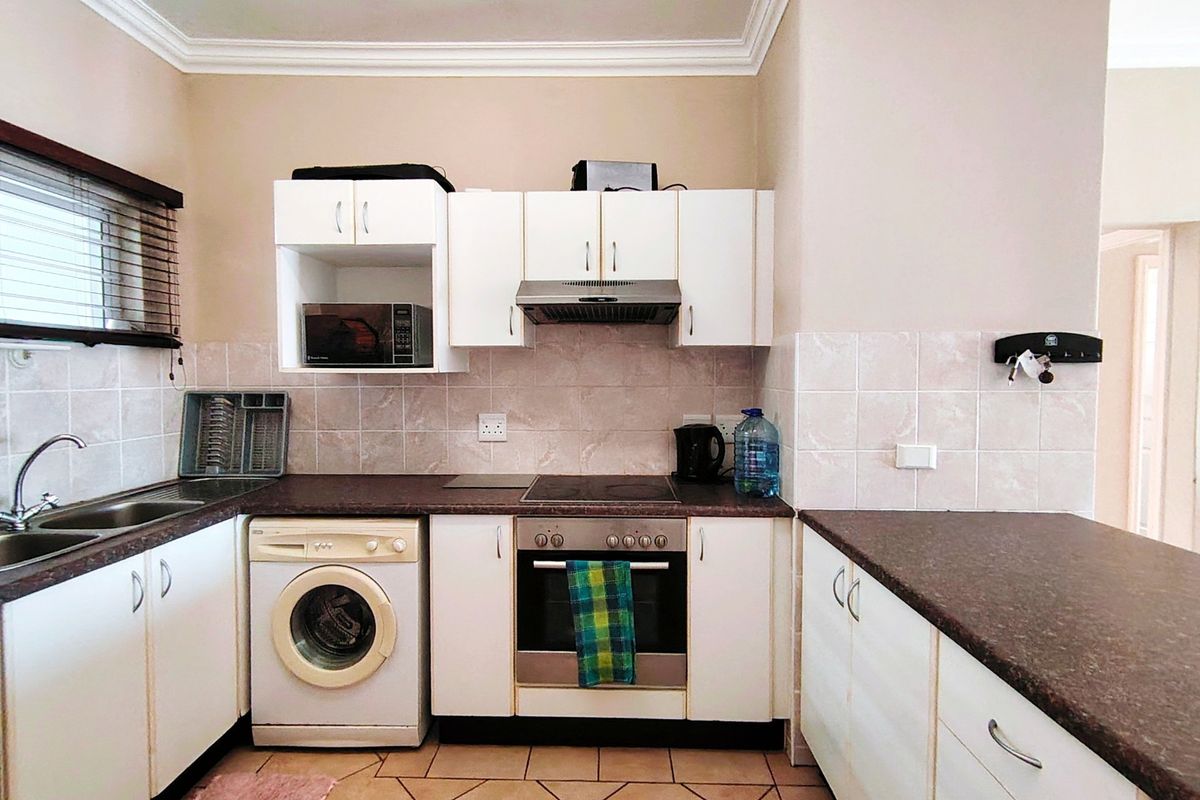 A functional kitchen featuring white cabinetry, dark laminate countertops, tiled backsplash, and integrated appliances including an oven, hob, and extractor fan.