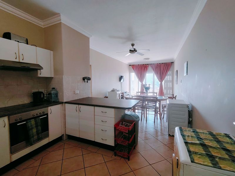 Open-plan kitchen and dining area featuring tiled floors, built-in cabinetry, and a breakfast counter, leading to a bright living space with balcony access.