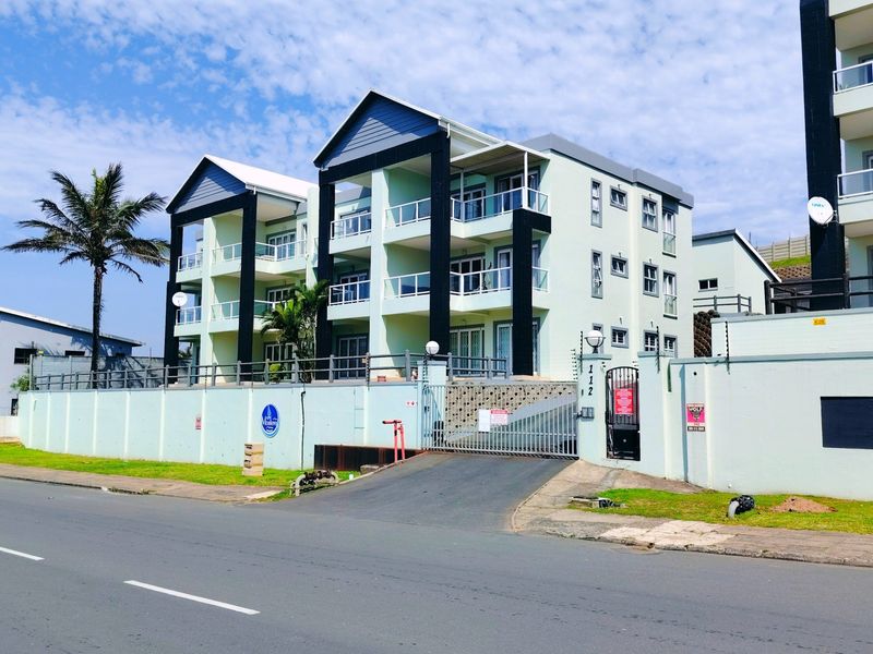 Front exterior view of a multi-story apartment complex featuring balconies, a secure gated entrance, and perimeter wall with electric fencing.