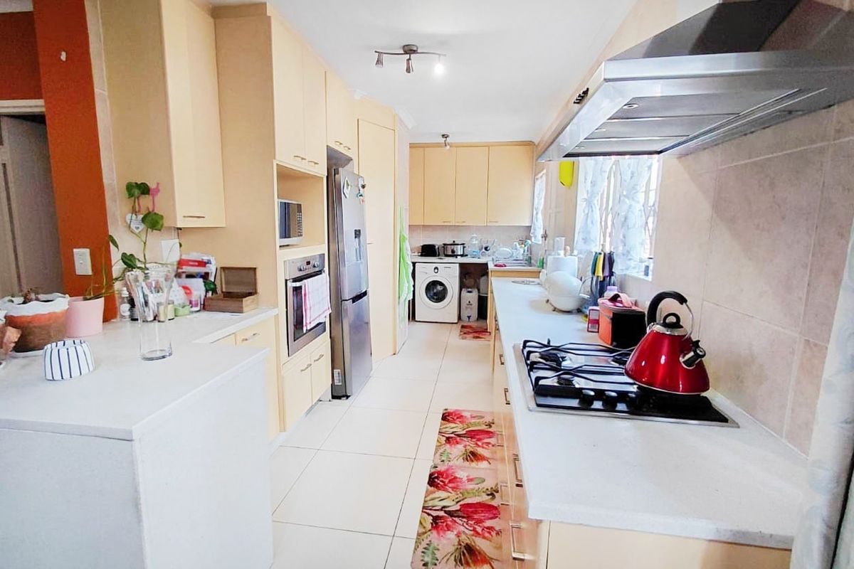 A functional kitchen featuring light-toned cabinetry, stone countertops, a gas hob with extractor fan, and integrated laundry facilities.