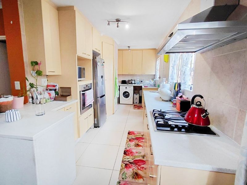 A functional kitchen featuring light-toned cabinetry, stone countertops, a gas hob with extractor fan, and integrated laundry facilities.