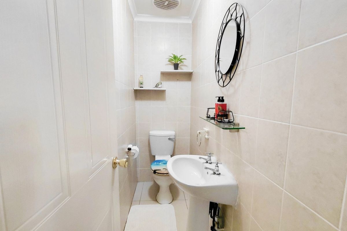 A compact guest bathroom featuring a pedestal basin, toilet, and neutral wall tiling with built-in shelving.