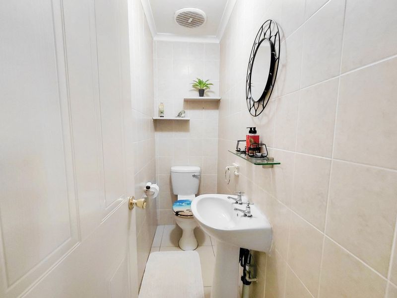 A compact guest bathroom featuring a pedestal basin, toilet, and neutral wall tiling with built-in shelving.
