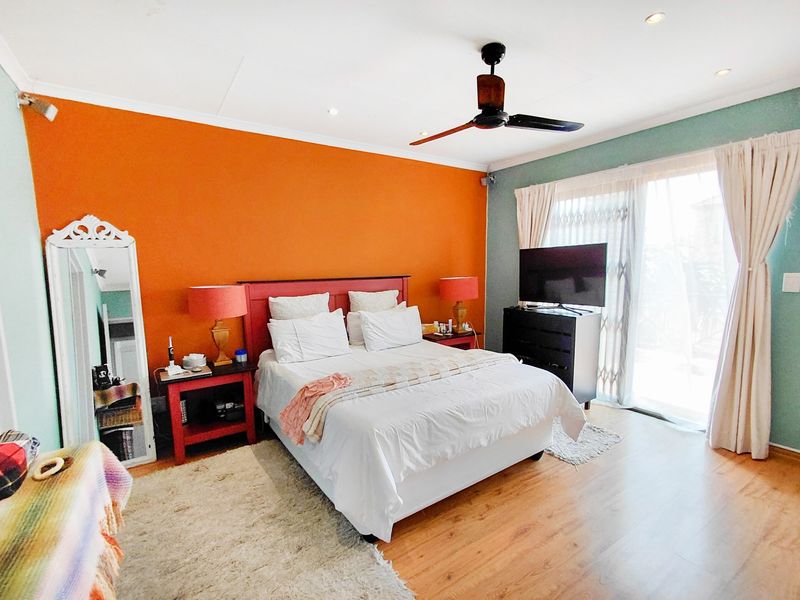 A spacious bedroom featuring laminate flooring, a ceiling fan, and a sliding glass door providing access to the exterior.