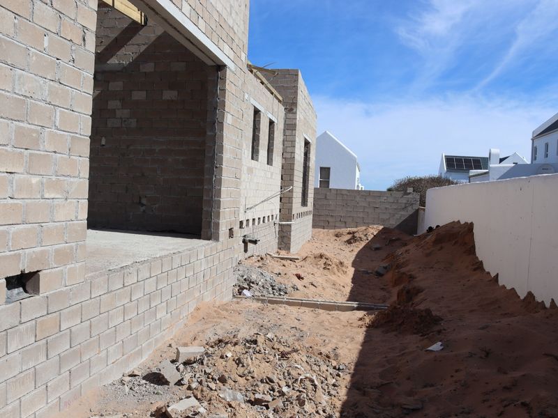 Rear view of a residential property currently under construction, featuring exposed concrete block walls and an unfinished yard area.