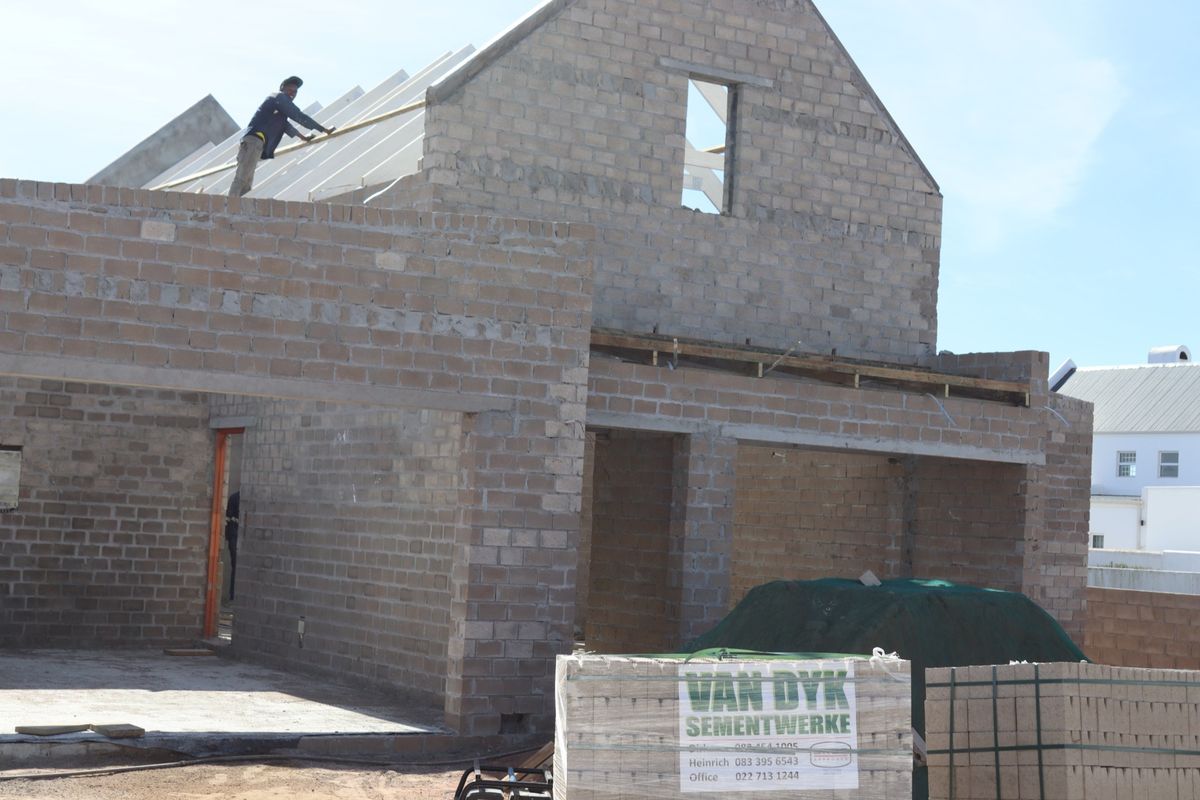 A residential property under construction, featuring exposed concrete block walls and roof trusses in the early stages of development.
