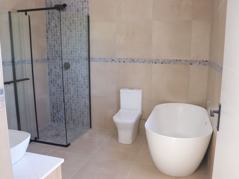 Modern bathroom featuring a freestanding bathtub, a walk-in shower with a glass screen, a toilet, and a vanity basin with neutral wall and floor tiling.