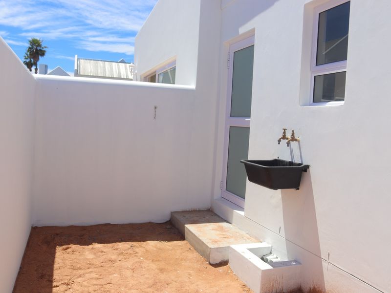A clean rear exterior courtyard area featuring a utility sink, external water taps, and a concrete step leading to a frosted glass door.