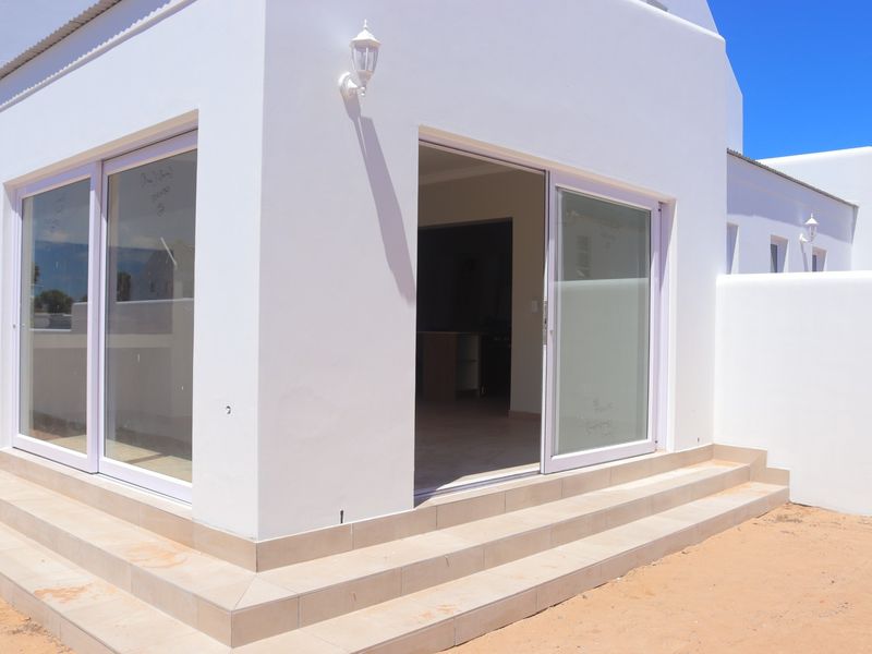 Rear exterior view of a modern white house featuring sliding glass doors and tiled steps leading to an outdoor area.