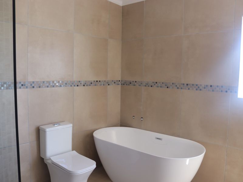 Modern bathroom featuring a freestanding bathtub, toilet, and neutral wall tiling with a decorative mosaic border.