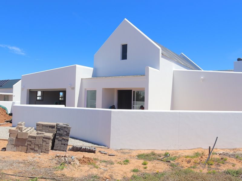 Modern white gabled house exterior featuring a clean architectural design, integrated garage, and boundary wall, currently undergoing final landscaping and site completion.