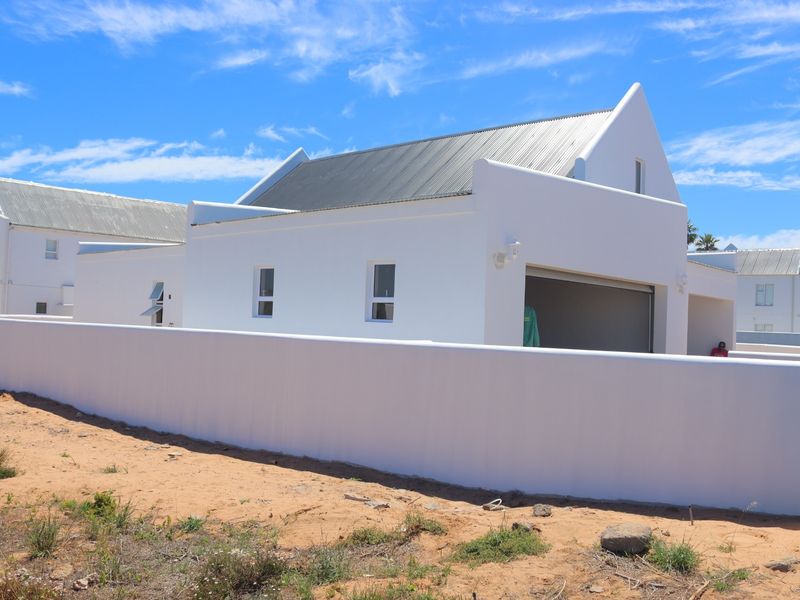 A modern white house with a distinctive gabled roof, featuring a garage and a clean boundary wall, set against a clear blue sky.
