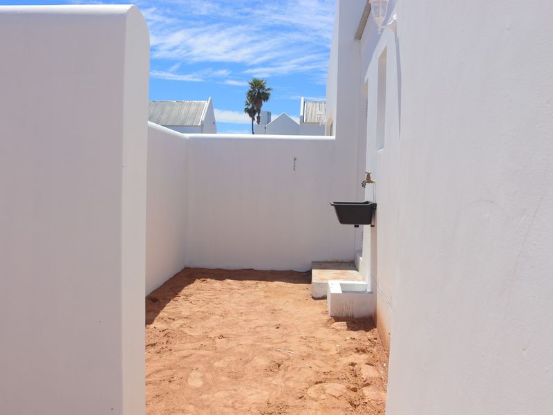 A private outdoor courtyard area featuring white masonry walls, a functional outdoor sink, and an unfinished sandy ground surface.