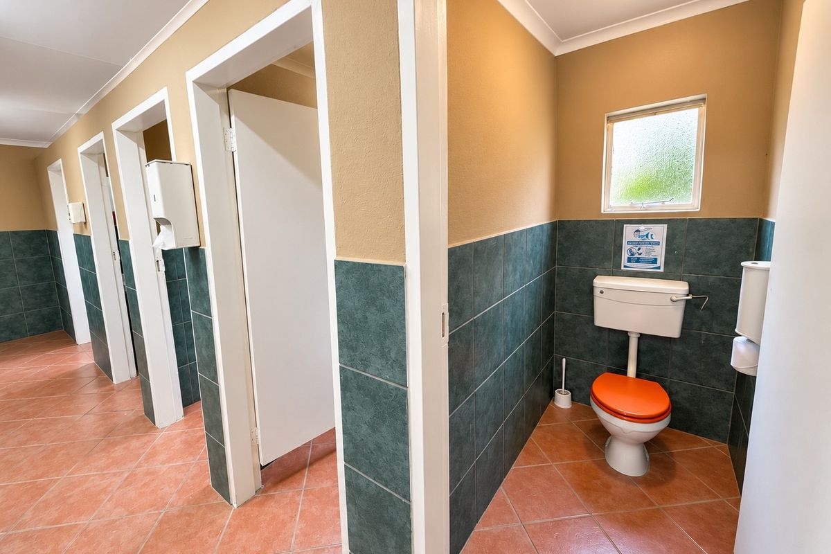A functional communal bathroom facility featuring multiple toilet cubicles, tiled flooring, and wall tiling with a neutral color scheme.