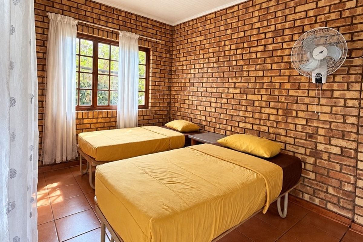 A bedroom featuring exposed brick walls, tiled flooring, and a wall-mounted fan, providing a rustic lodge-style aesthetic.