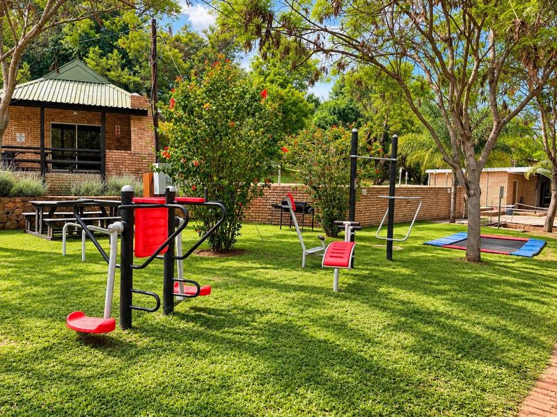 Outdoor fitness area featuring fixed exercise equipment set within a well-maintained garden space, adjacent to a brick-built lodge structure.