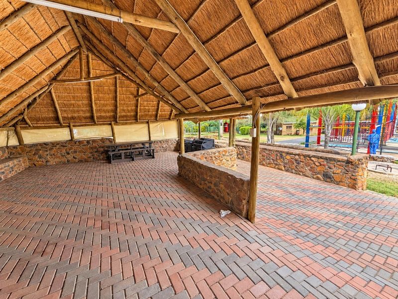 A spacious covered outdoor patio featuring a traditional thatched roof, stone-clad walls, and durable brick paving, ideal for lodge-style entertainment.