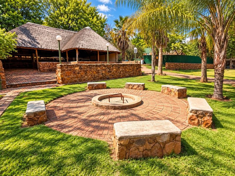 Outdoor entertainment area featuring a circular brick fire pit with built-in stone seating, set within a landscaped garden near a thatched-roof structure.