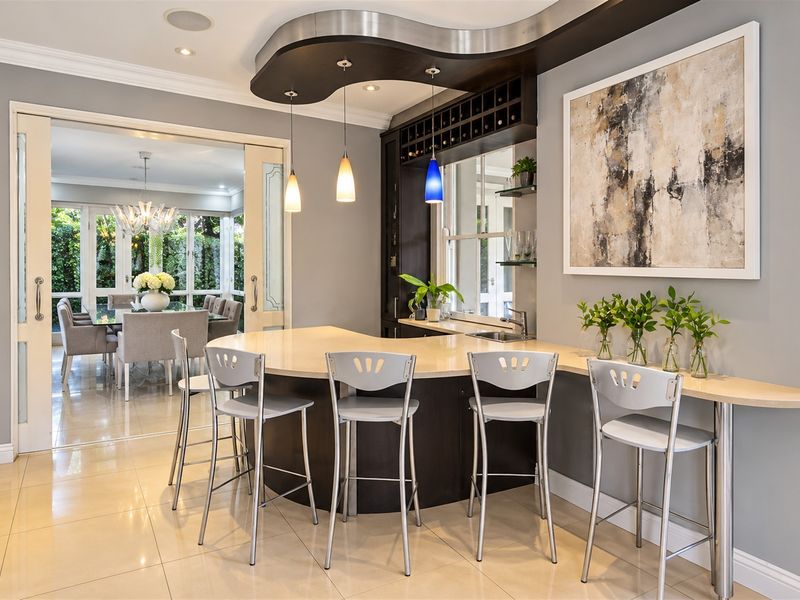 A sophisticated built-in bar area featuring a curved counter, integrated wine storage, and an undermount sink, seamlessly connected to the dining room via sliding doors.