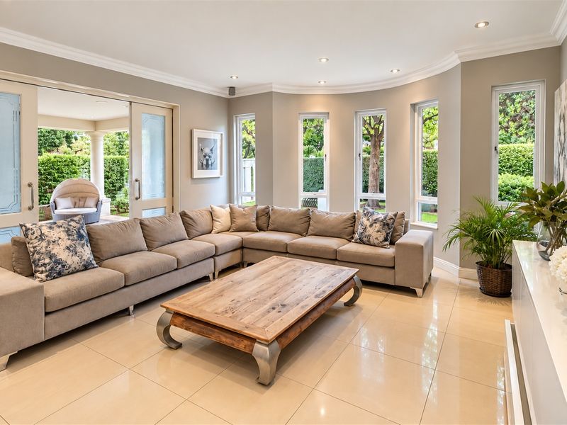A bright and spacious living room featuring polished tile floors, recessed lighting, crown molding, and large windows with direct access to an outdoor patio area.