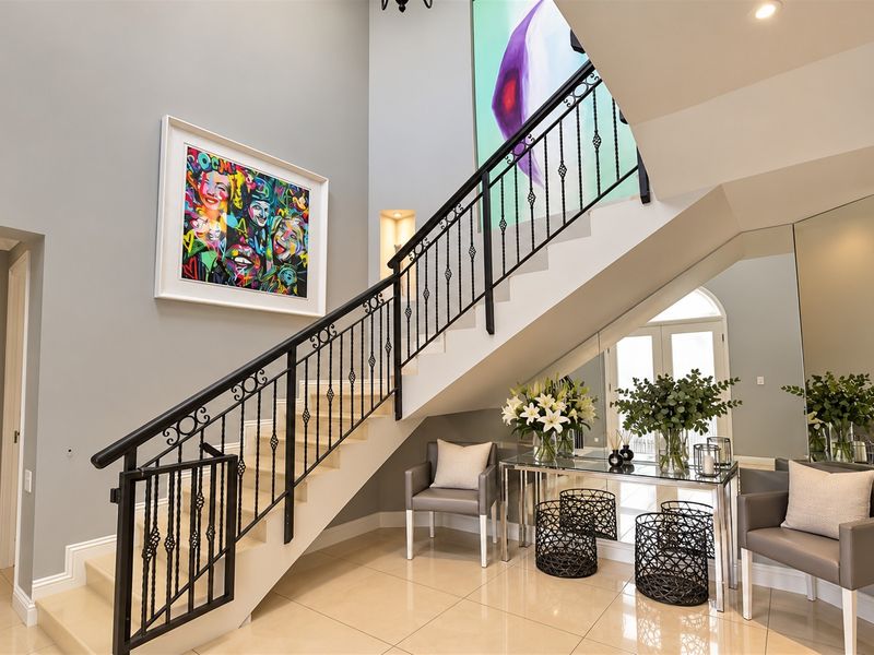 Elegant double-volume entrance hall featuring a grand staircase with decorative wrought iron railings, polished tile flooring, and sophisticated mirrored accents.