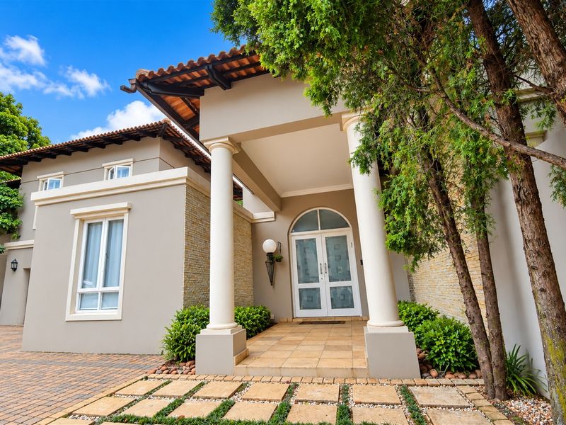 A well-maintained front entrance featuring a covered porch with classical columns, stone cladding accents, and a paved driveway.