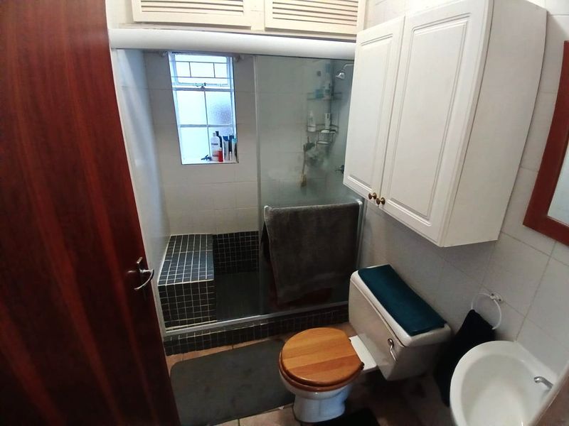 A functional bathroom featuring a walk-in shower with a tiled bench, a wall-mounted storage cabinet, a pedestal basin, and a toilet.