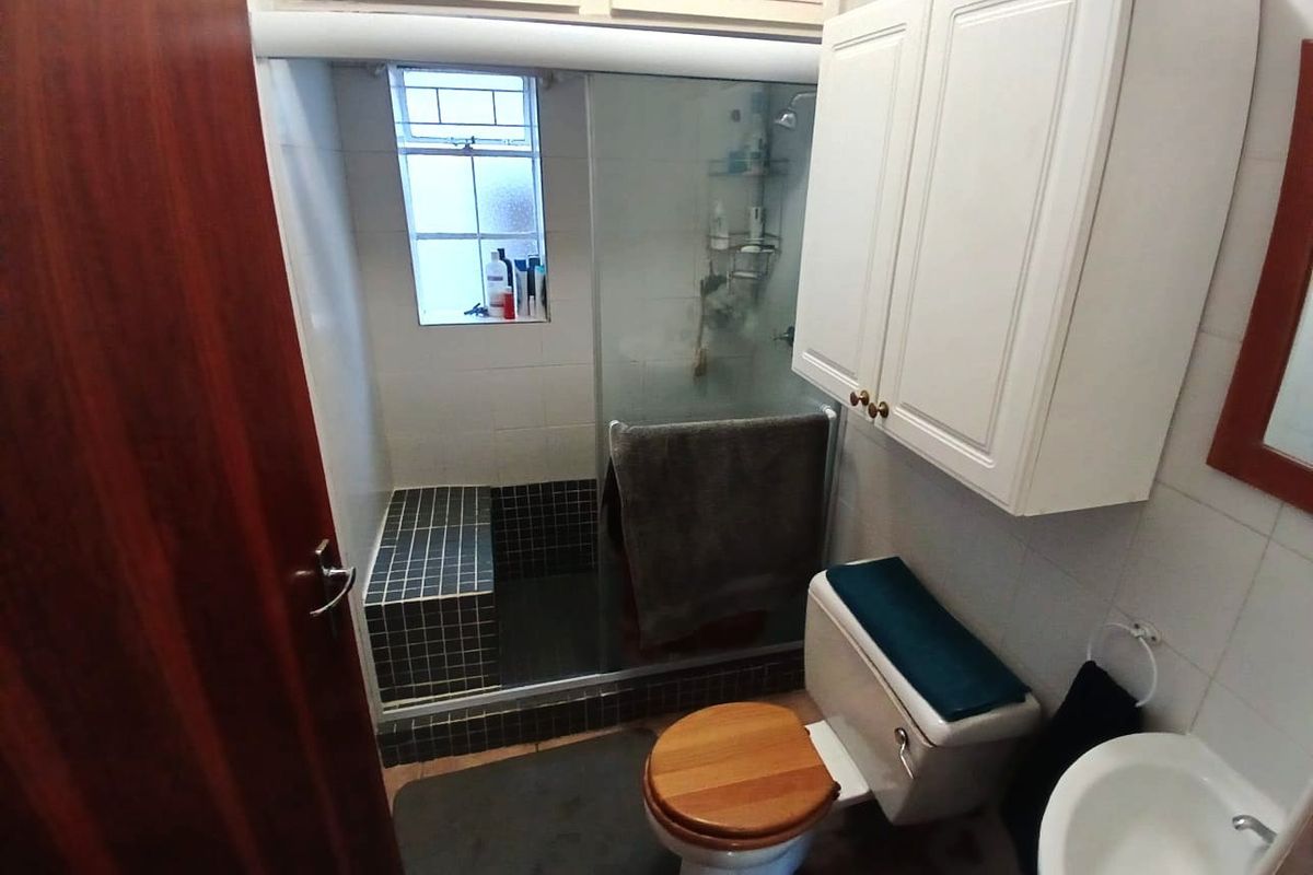 A functional bathroom featuring a walk-in shower with a tiled bench, a wall-mounted storage cabinet, a pedestal basin, and a toilet.
